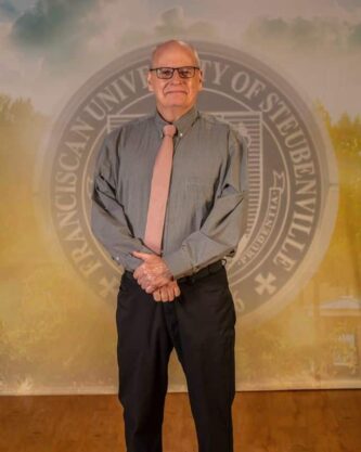Dr Timothy Williams 2025 Dr. Timothy Williams in professional wear standing in front of the university seal.