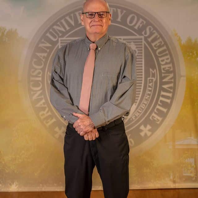 Dr Timothy Williams 2025 Dr. Timothy Williams in professional wear standing in front of the university seal.