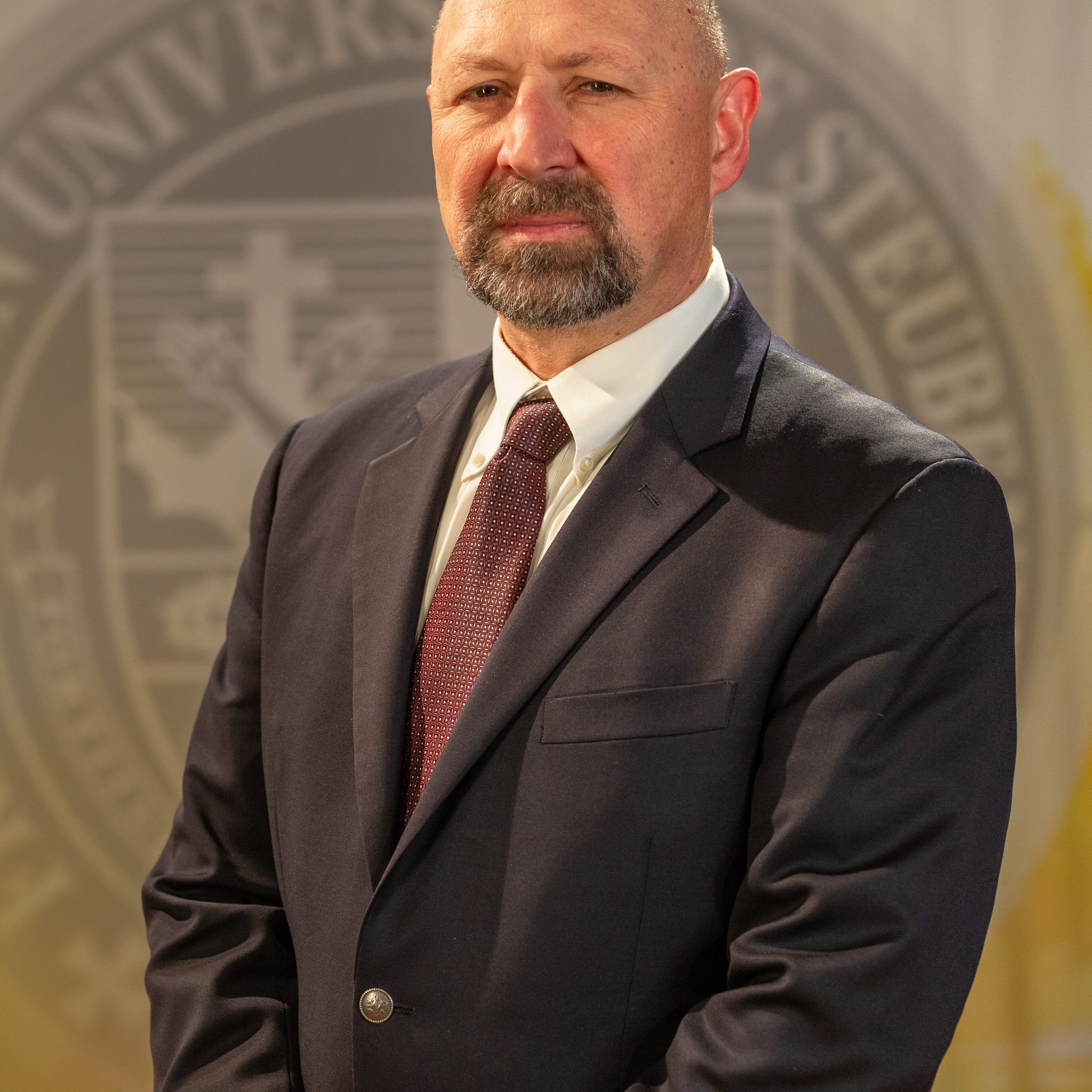Faculty portrait of Dr. Aaron Urbanczyk standing in front of the Franciscan University of Steubenville seal.