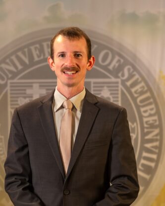 Taylor Caputo standing in front of the Franciscan University of Steubenville seal.